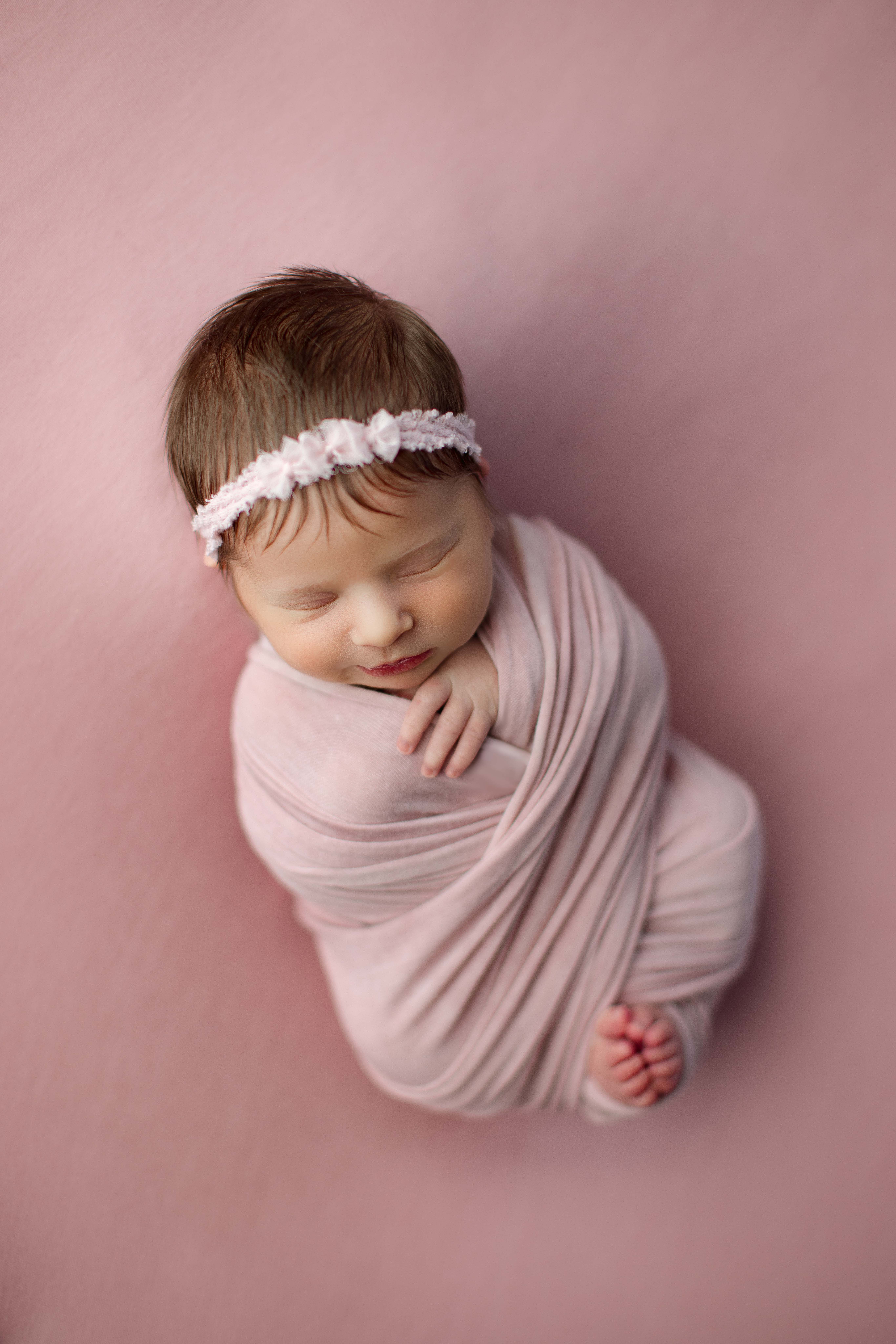 Newborn baby girl in pink criss cross wrap with pink headband