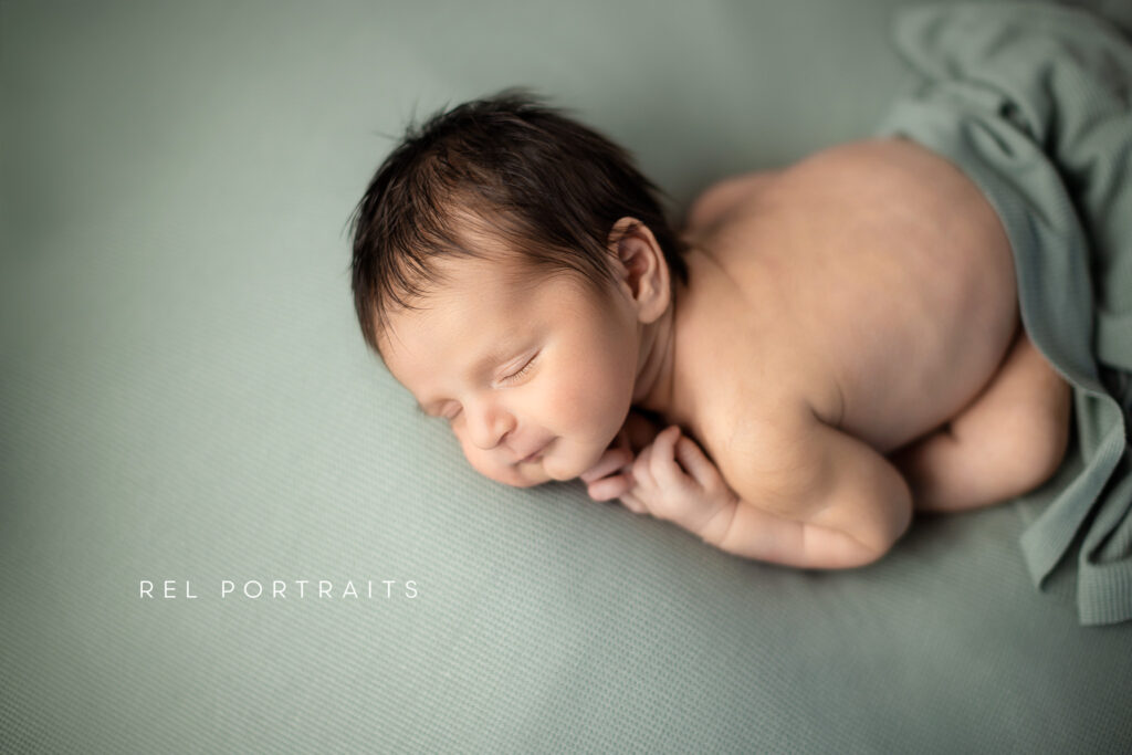 Baby boy in sage green smiling for newborn photography