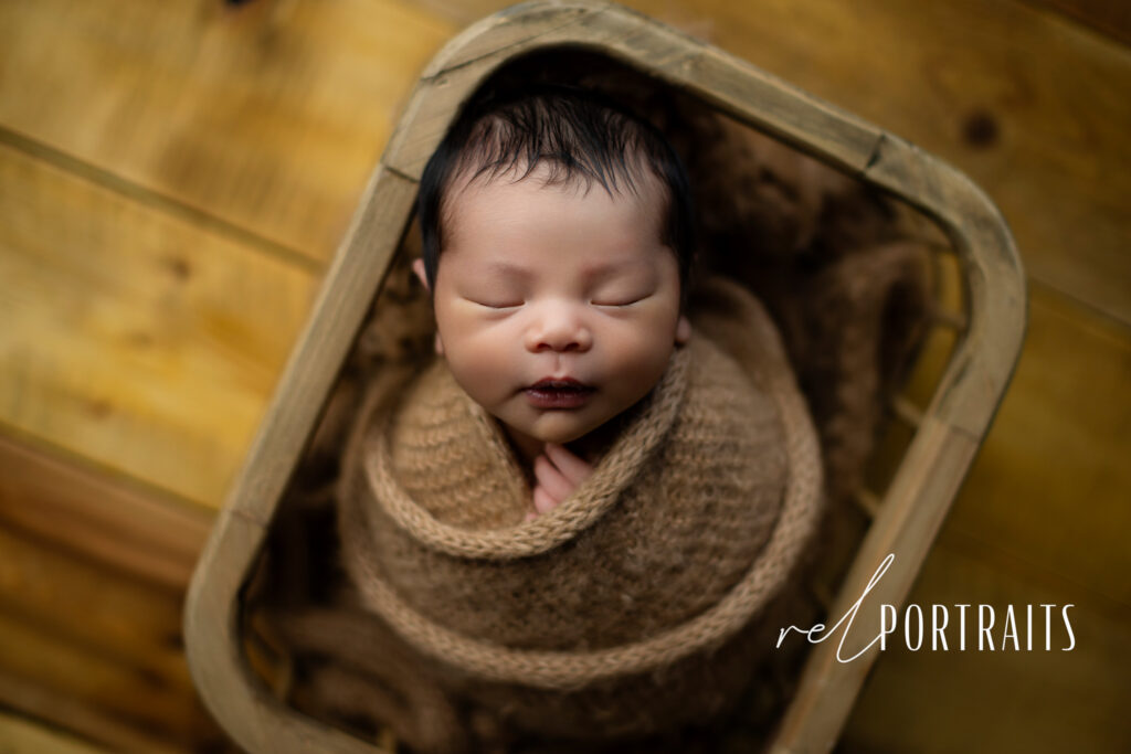 newborn wrapped in brown ball at photoshoot