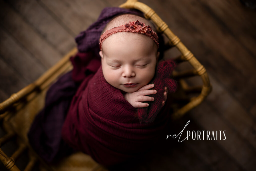 newborn baby girl in burgundy holding a baby bear 